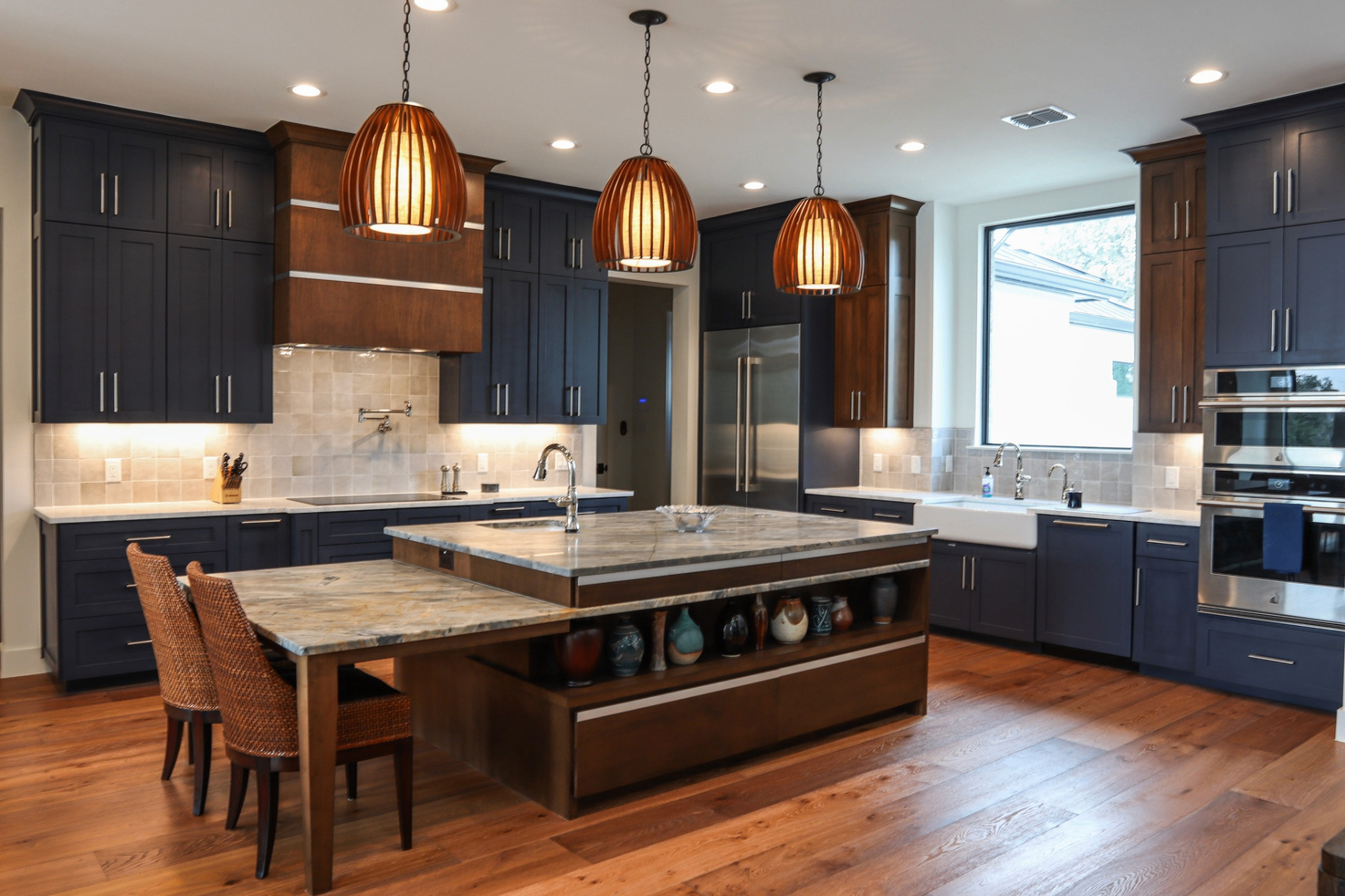 Navy and walnut two-tone kitchen with dual islands, farmhouse sink, and woven pendant lighting by Amaya