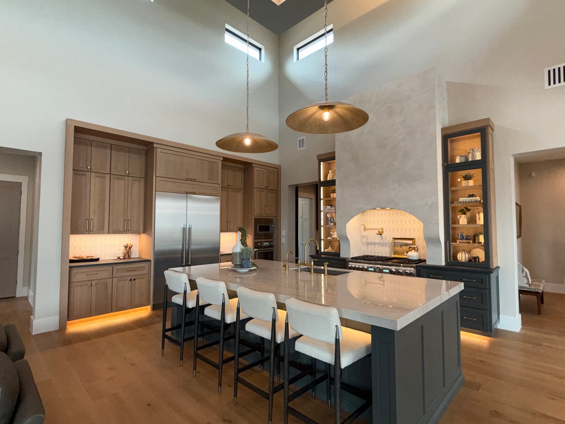 Two-story great room kitchen with rift-sawn white oak cabinetry, graphite island, and brass pendants by Amaya