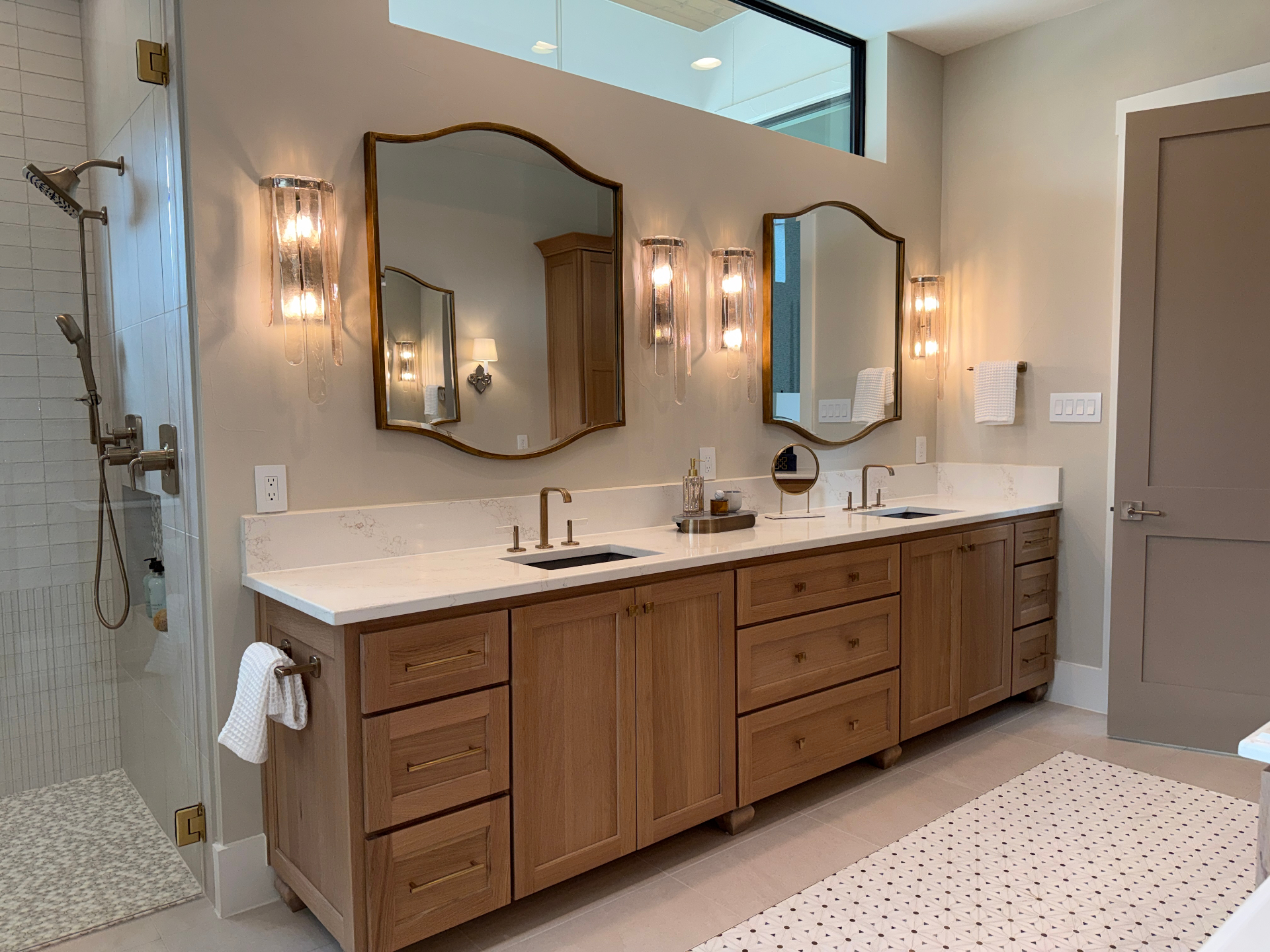 Primary bath with white oak dual vanity, quartz counters, and arched brass mirrors by Amaya