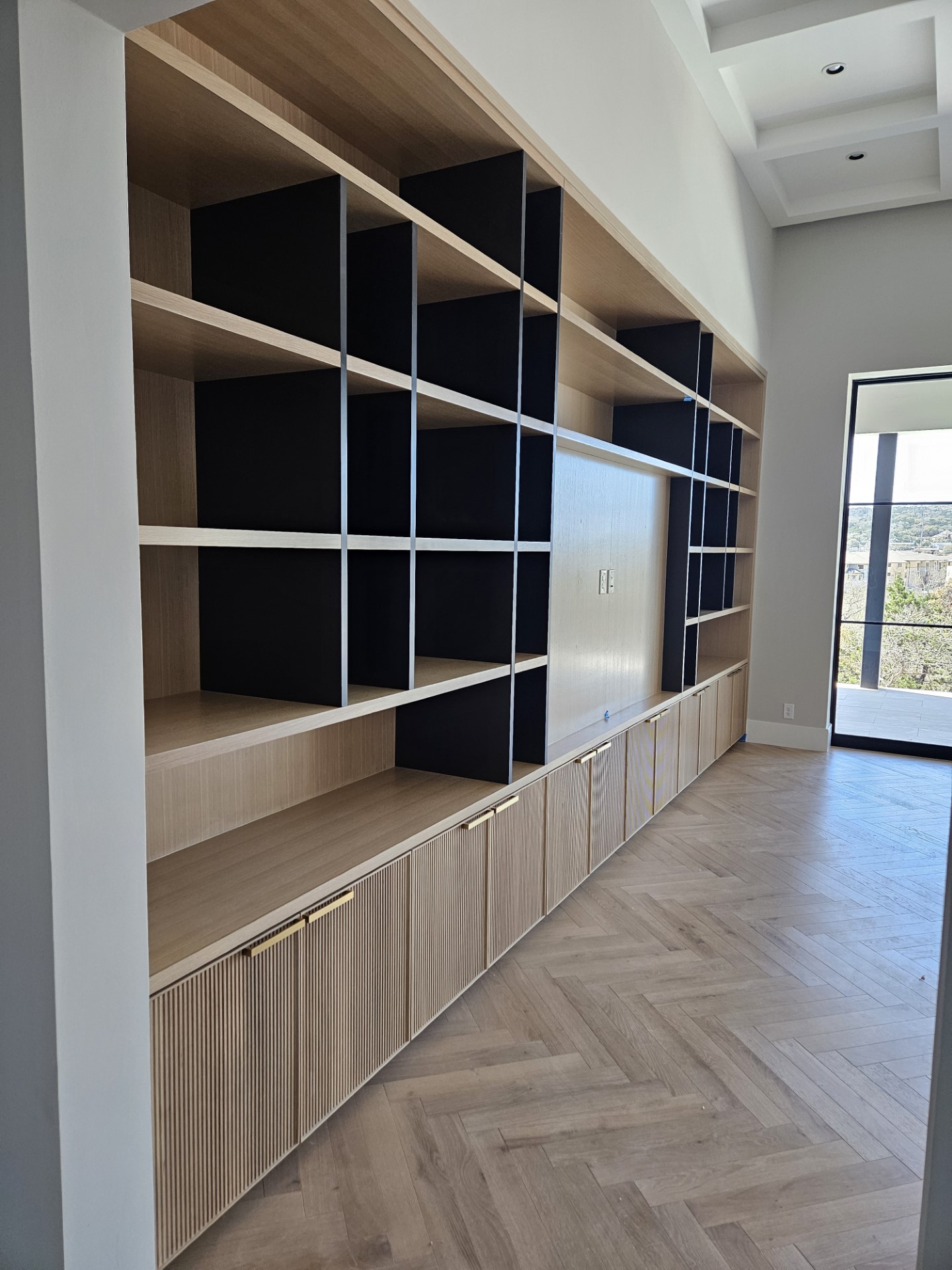 Angled view of white oak built-in shelving with fluted base doors and brass pulls by Amaya