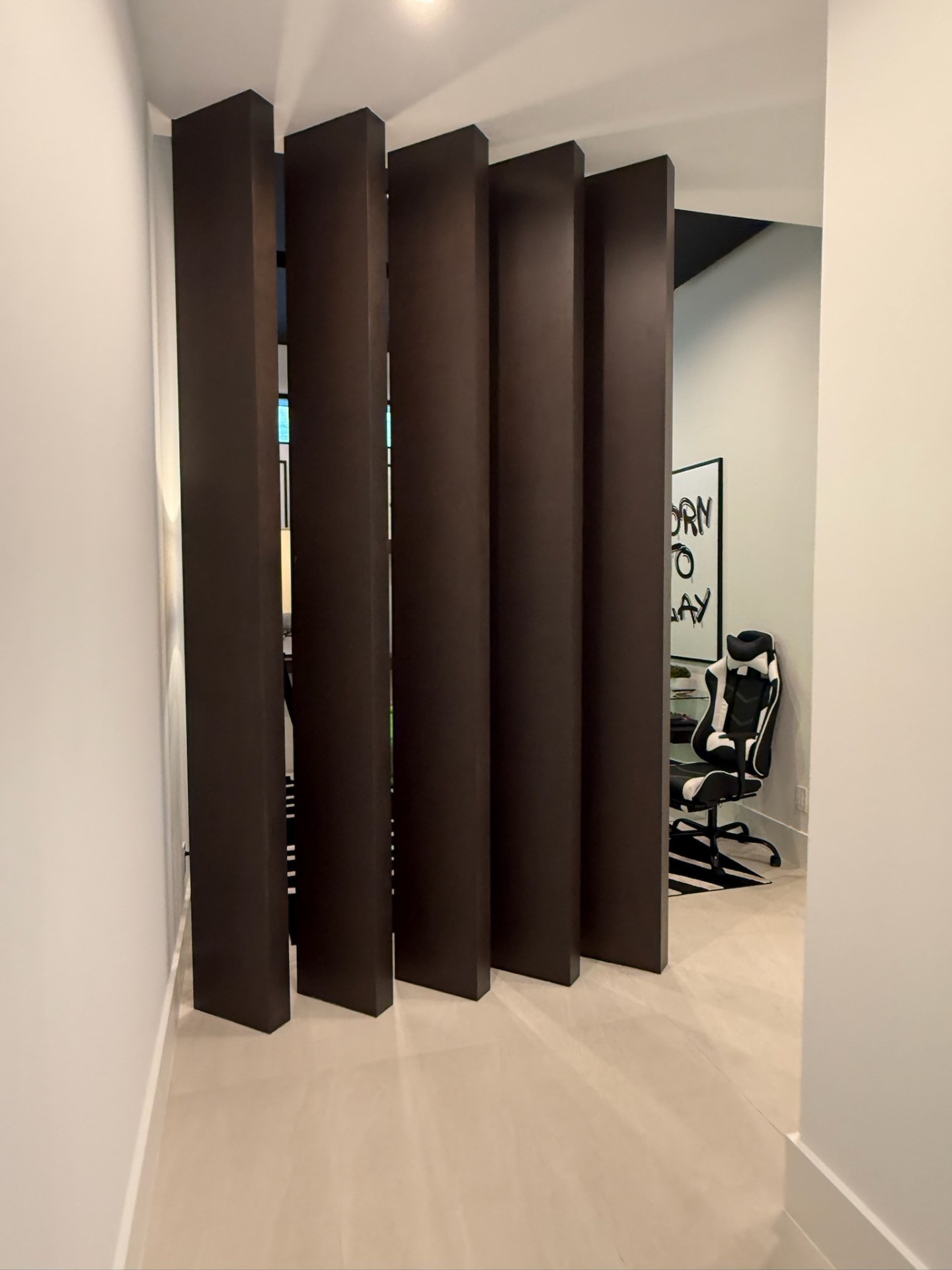 Architectural walnut slat room divider separating a study from an adjacent living space by Amaya