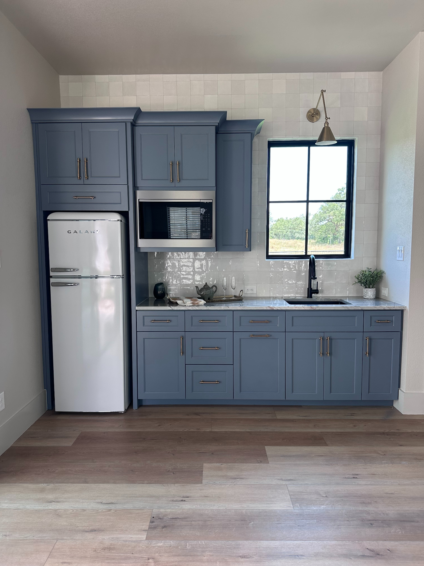 Kitchenette with slate blue full-overlay cabinetry, brass hardware, and marble counters by Amaya