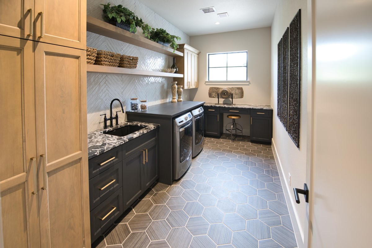 Custom laundry and mudroom with two-tone cabinetry, natural maple pantry tower, black shaker base, and hexagon tile flooring by Amaya