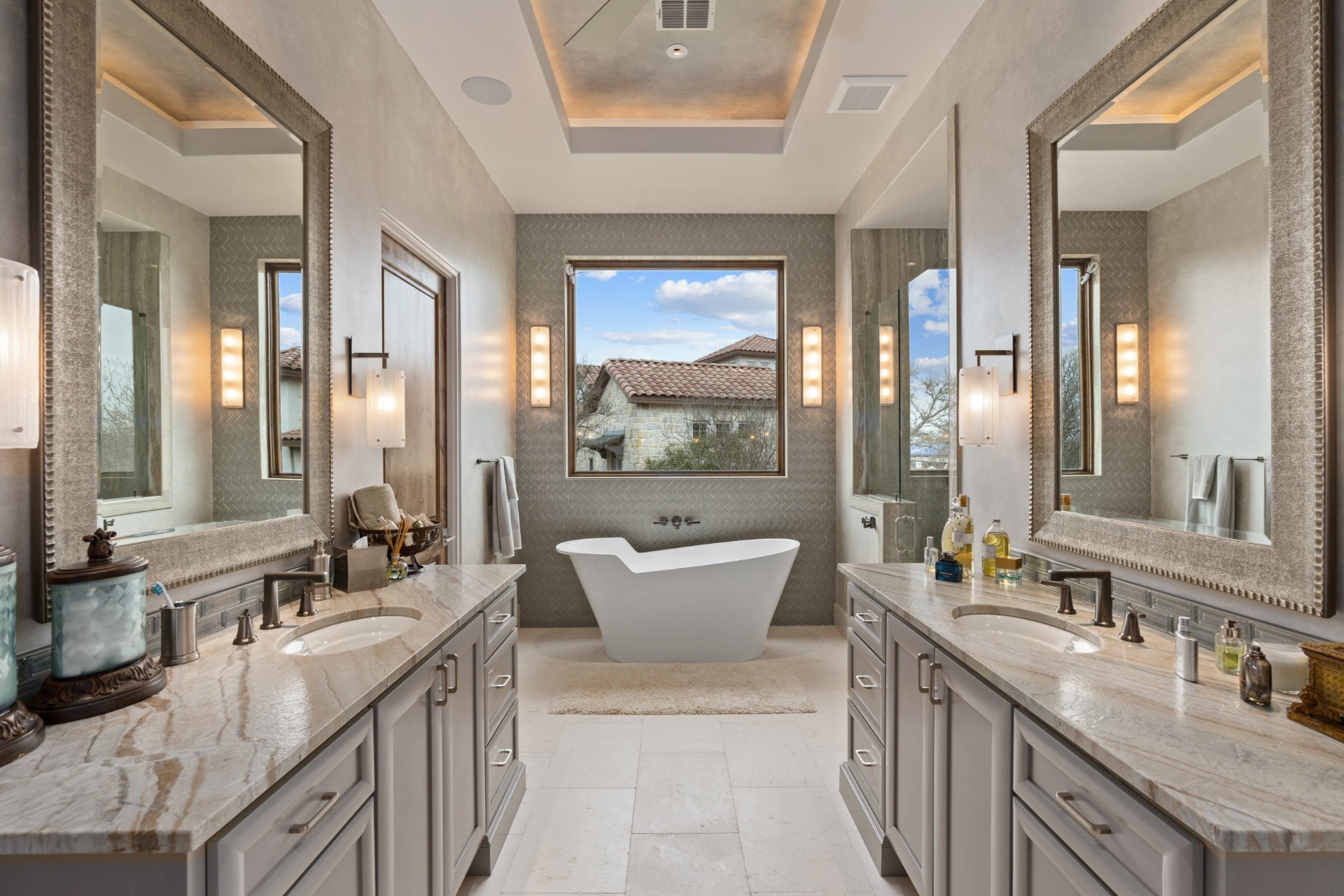 Mediterranean master bath with dual gray vanities, quartzite counters, and a freestanding soaking tub by Amaya