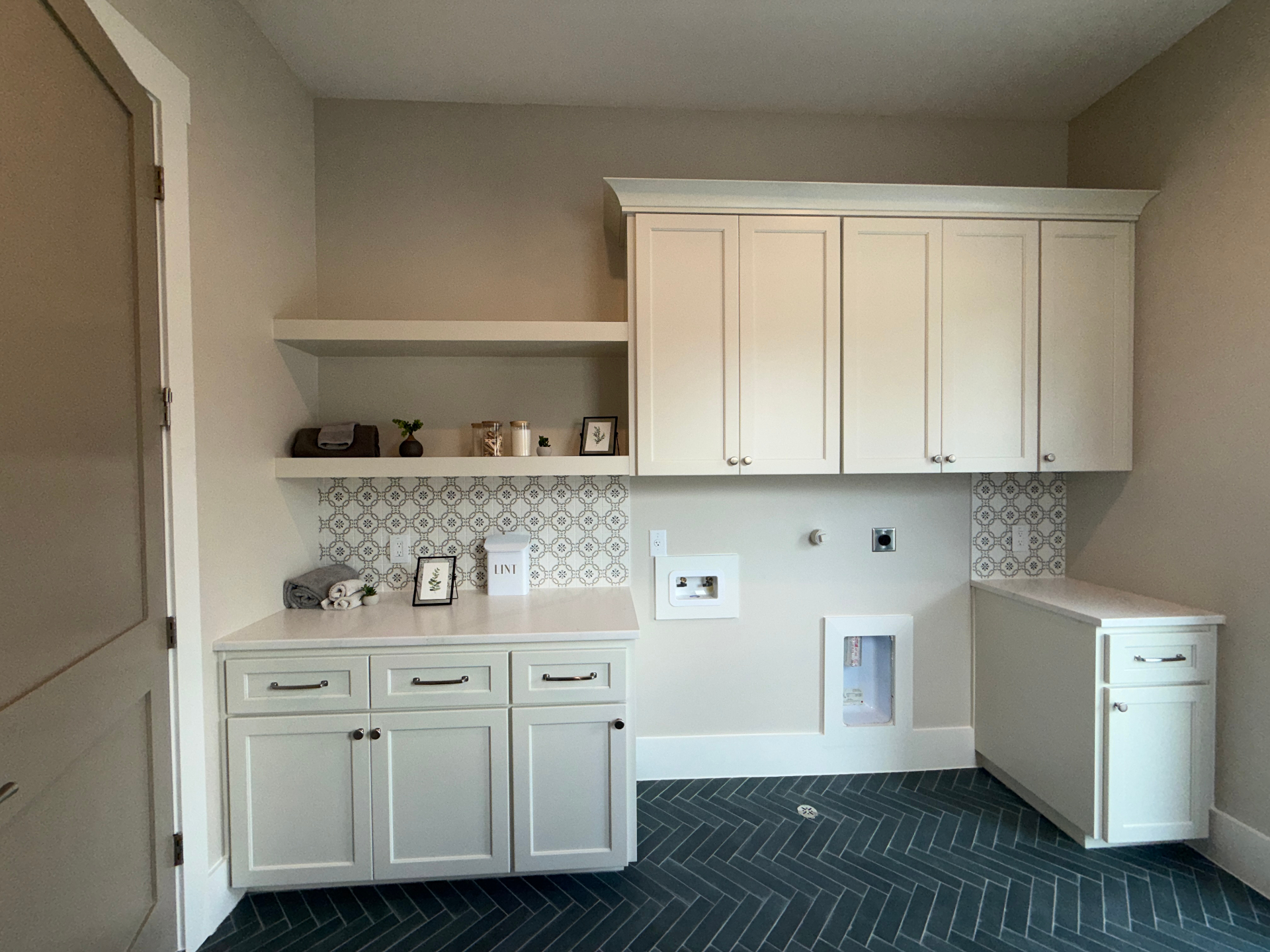 Painted laundry suite with shaker cabinetry, floating shelf, and blue herringbone tile floor by Amaya
