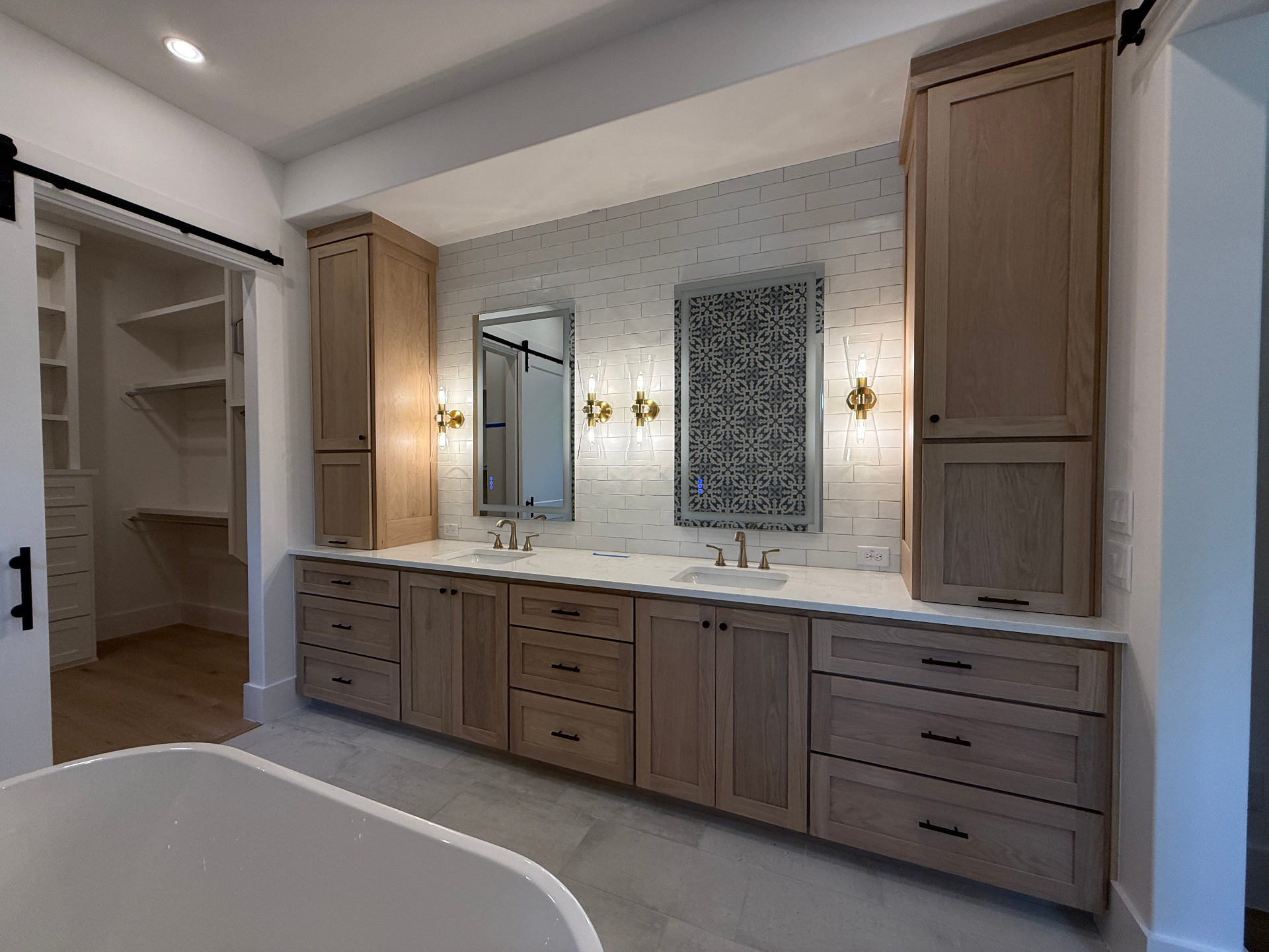 Master bath with natural white oak dual vanity, linen towers, subway tile, and patterned tile inset by Amaya