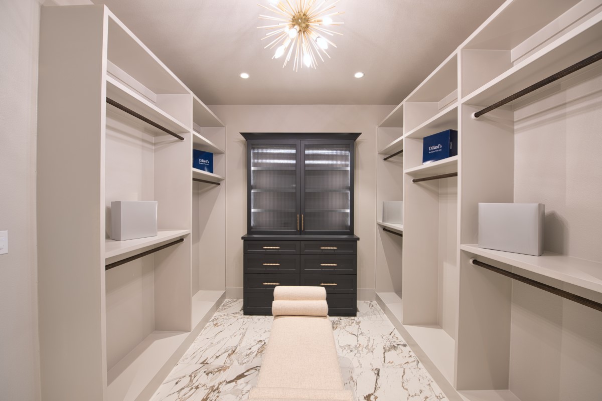 Custom walk-in closet in San Antonio with painted perimeter cabinetry, an espresso oak island dresser with fluted glass doors, and marble flooring by Amaya